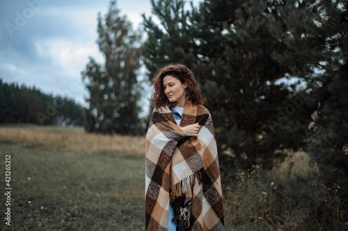 Attractive girl wrapped in a checkered plaid on a forest and field background