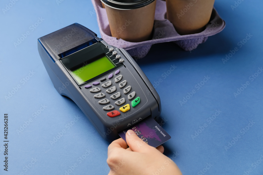 Female hand with payment terminal, credit card and takeaway cups on color background Female hand with payment terminal, credit card and takeaway cups on color background