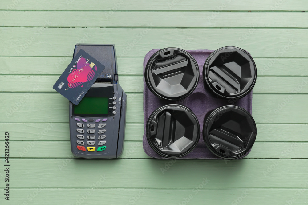 Payment terminal with credit card and takeaway cups on color wooden