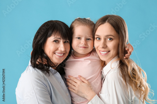 Young woman, her little daughter and mother on color background