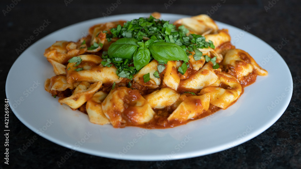 ready to eat, homemade tortelloni stuffed with prosciutto in tomato sauce with basil