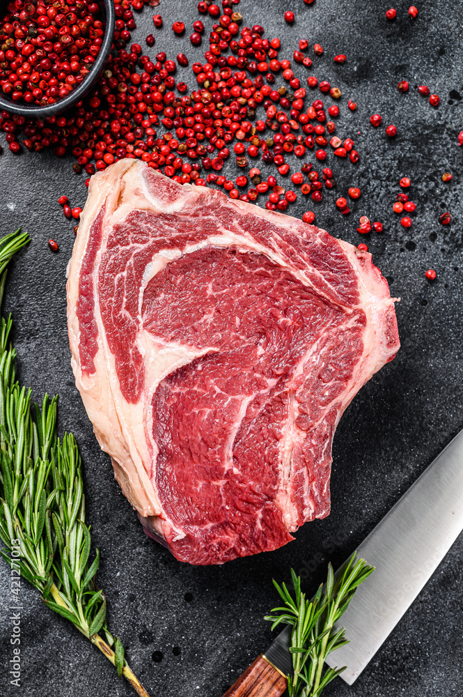 Raw cowboy steak or ribeye on the bone with herbs. Marble beef. Black background. Top view.