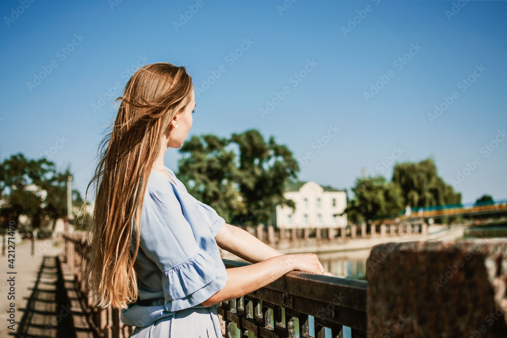 Summer Hair Care, Sunscreen for Hair, Conditioning. Blonde girl with long hair stands near river in the city in summer day