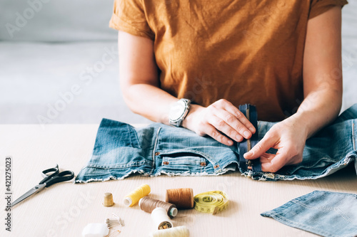 Woman repairs sews reuses fabric from old denim clothes economical reuse