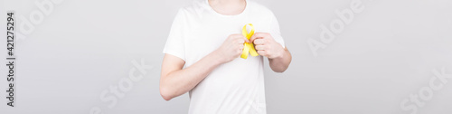 Young man in white t-shirt holding yellow ribbon awareness symbol for suicide, sarcoma bone cancer, bladder cancer, liver cancer and childhood cancer concept. Health care. Copyspace.