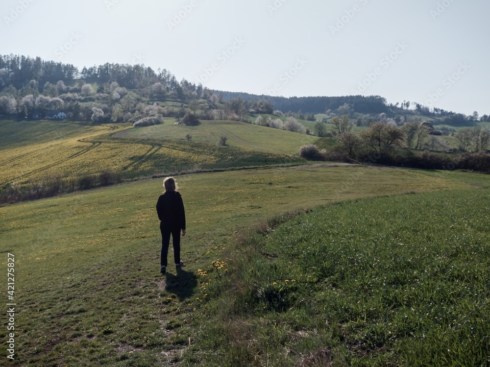 young woman walking towards the sun and hiking the forest hills far from the city