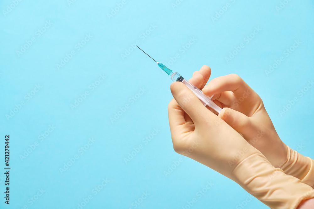 Doctor's hands in gloves hold a syringe with a needle on a blue background. Syringe and vial human hand about to make vaccine.Vaccines against pneumonia covid19. Doctor's hands in gloves hold a syringe with a needle on a blue background. Syringe and vial human hand about to make vaccine.Vaccines against pneumonia covid19.