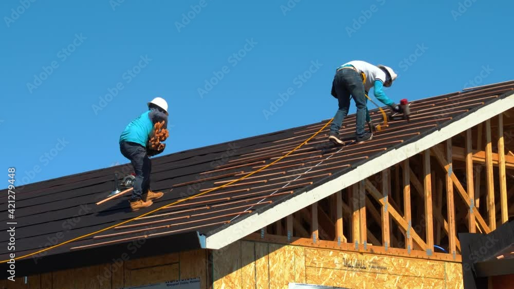 Two workers nailing wood slats for installation of ceramic roofing tiles on residential building using an air nail gun- new home roof construction in California shot in 4K