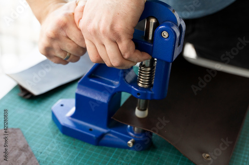 Artisan using hand press for setting snaps in leather for makes a wallet. Hand Pressure Snap Pressing Machine is using by craftsman in leather workshop.