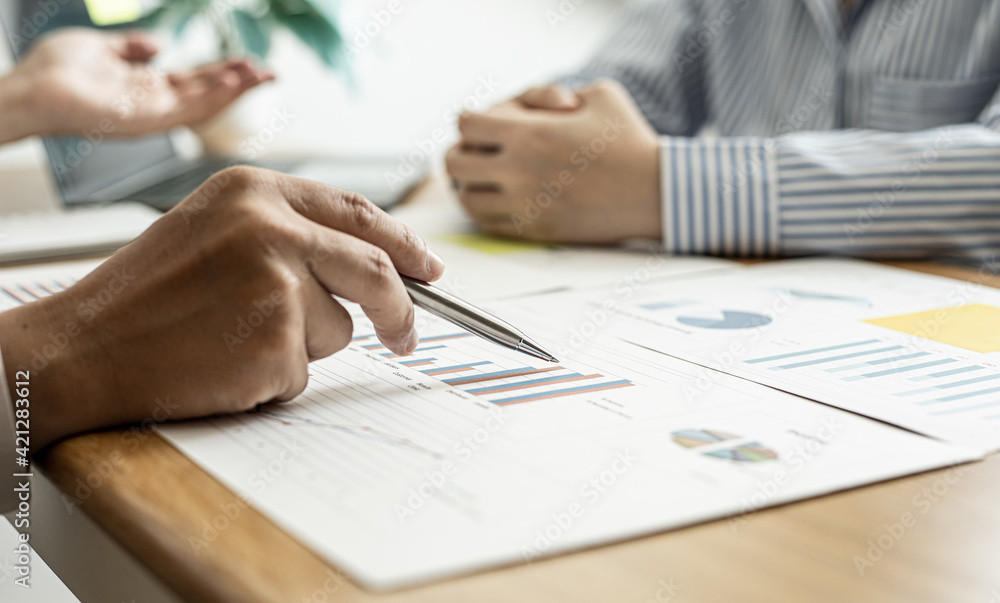 A close-up of a financial businessman holding a pen and pointing at the information sheet on his desk, reading the company's financials to make a financial plan. Financial concept. A close-up of a financial businessman holding a pen and pointing at the information sheet on his desk, reading the company's financials to make a financial plan. Financial concept.