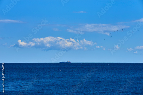 distant cargo ship in horizon with high clouds and calm sea and seagulls in sky