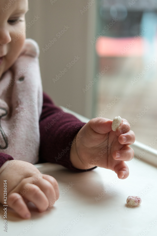 Young baby using pincer grasp to pick up cereal puff; developmental