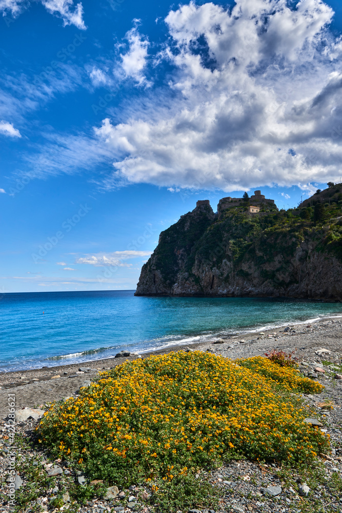 the beach of Eastern Sicily under Taromina in Sicily in a day of clouds and blue sky with spring blooms