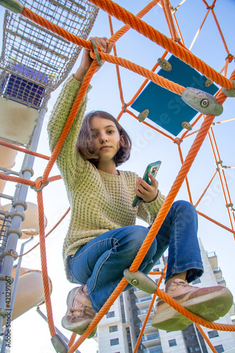 Cute European Beautiful natural teenage girl looks through the rope web on playground. © Kira