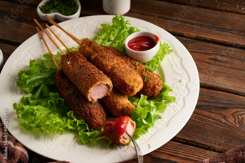 Tasty corn dog with sauce and salad served on white plate