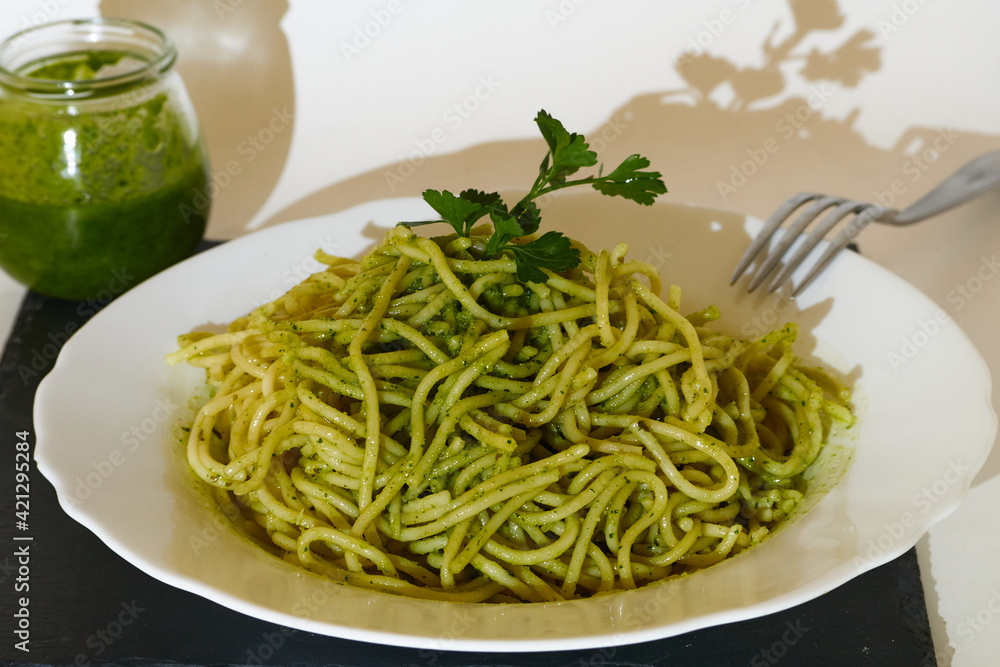 Tasty Spaghetti with pesto sauce and a parsley leaf in a plate and a glass of pesto Sauce
