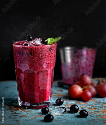 grape and black currant smoothie in transparent glass front view on old wooden blue table on dark background closeup. Selective focus
