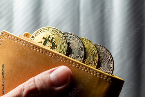 Mão segurando carteira cheia de tokens de Bitcoins. Criptomoedas ouro e prata com fundo desfocado.