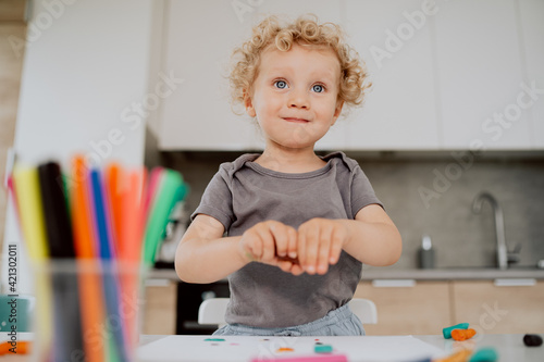 Portrait of a lovely happy preschool-aged girl sitting at her kitchen table enjoying some free time. Little cute girl is making something out of plasticine.