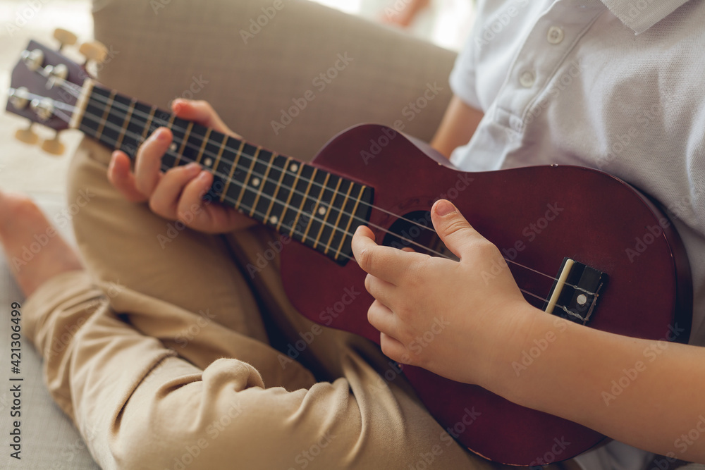 Little boy plays the ukulele. Home teaching music. Quarantine.