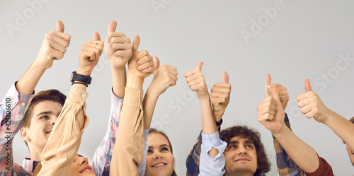 Cropped image of young men and women raising hands in the air and raising thumbs up on gray background. Team of students with a happy expression makes a gesture of approval. Banner. Place for text.