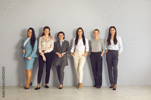 Team of young smiling businesswomen corporate partners employees standing together and looking at camera over grey wall background in office. Women working in company concept