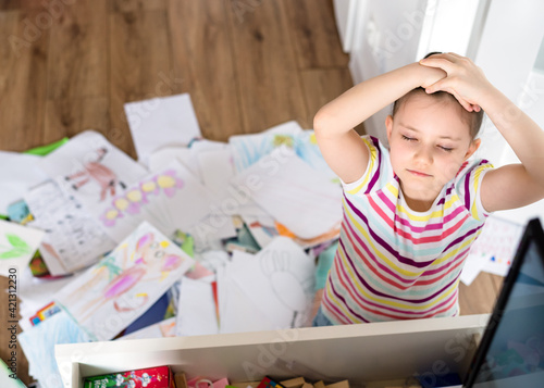 A preschool girl tidies up the dresser in her room. A child among a mess of a heap of papers, sheets and drawings