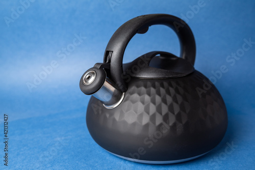 black metal teapot with whistle and plastic handle on blue background