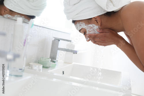 African american woman washing off her face mask in the sink at bathroom photo