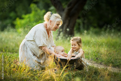 Fototapeta Naklejka Na Ścianę i Meble -  Old woman and little girl bathe a baby in basin outdoor