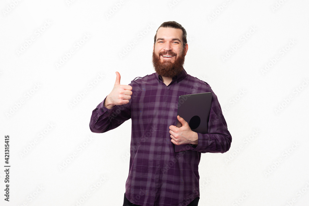 Photo of happy bearded student man showing thumb up and holding laptop Photo of happy bearded student man showing thumb up and holding laptop