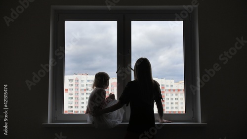 Mother comes to her lonely daughter who is sitting by the window.