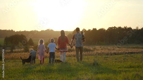 A large friendly family walks across the field at sunset with dog.