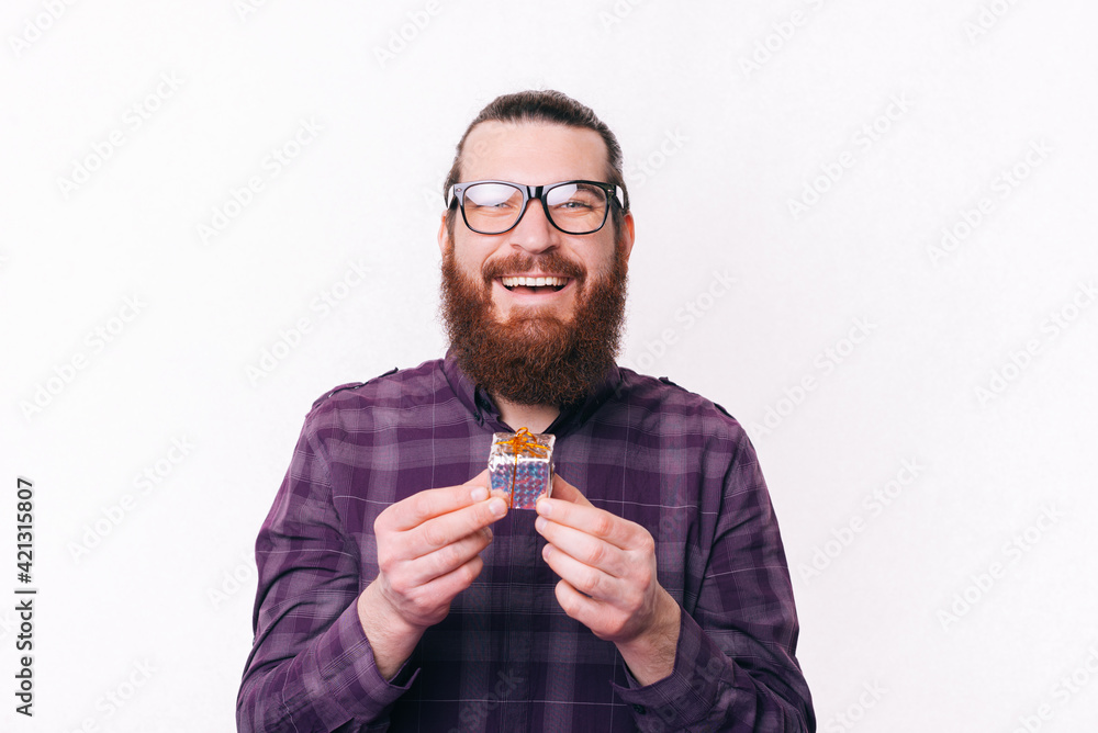 Portrait of cheerful young man with beard wearing eyeglasses and holding small gift Portrait of cheerful young man with beard wearing eyeglasses and holding small gift