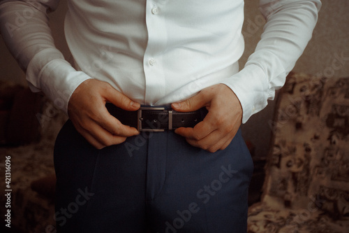 business man in shirt dresses and straightens leather belt close-up