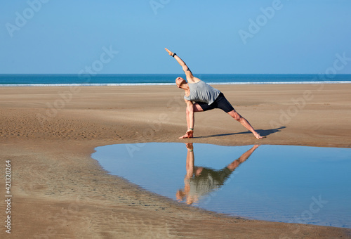 Man (40-44 years old) performing 'extended side angle' yoga pose on deserted beach in Woolacombe, North Devon