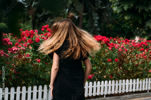 Young woman in a black dress. Spins with hair, on a background of red roses