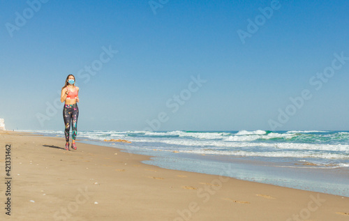 Girl running sport in the beach with covid mask and a blue sky and a blue sea with whit waves.