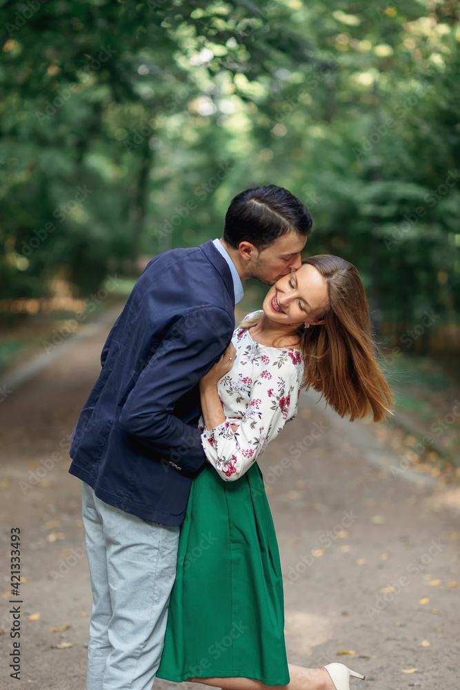 Beautiful smiling couple enjoying a walk in the city park. A man kisses a woman on the cheek. Beautiful smiling couple enjoying a walk in the city park. A man kisses a woman on the cheek.