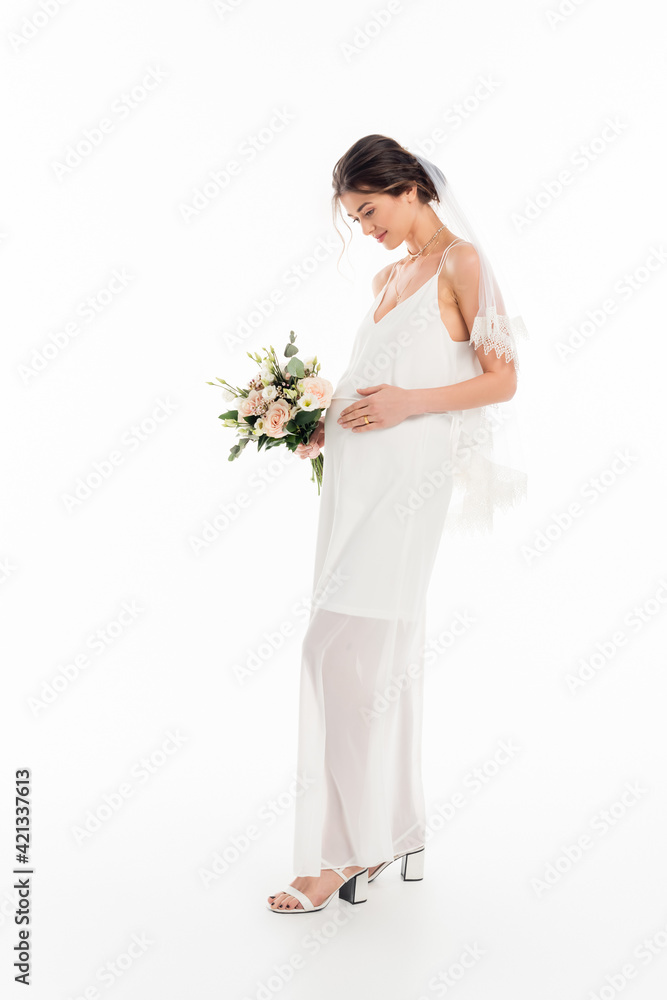 full length view of pregnant bride touching belly while holding bouquet on white full length view of pregnant bride touching belly while holding bouquet on white