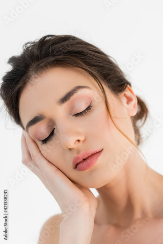 pretty woman with natural makeup touching face while posing with closed eyes isolated on white