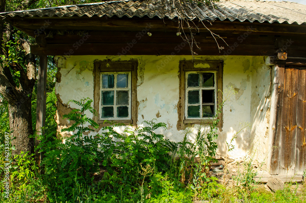 Old wooden rustic house plastered with clay and painted with white clay among flowering meadow grasses. House with cracked clay walls and wooden windows. Old wooden rustic house plastered with clay and painted with white clay among flowering meadow grasses. House with cracked clay walls and wooden windows.