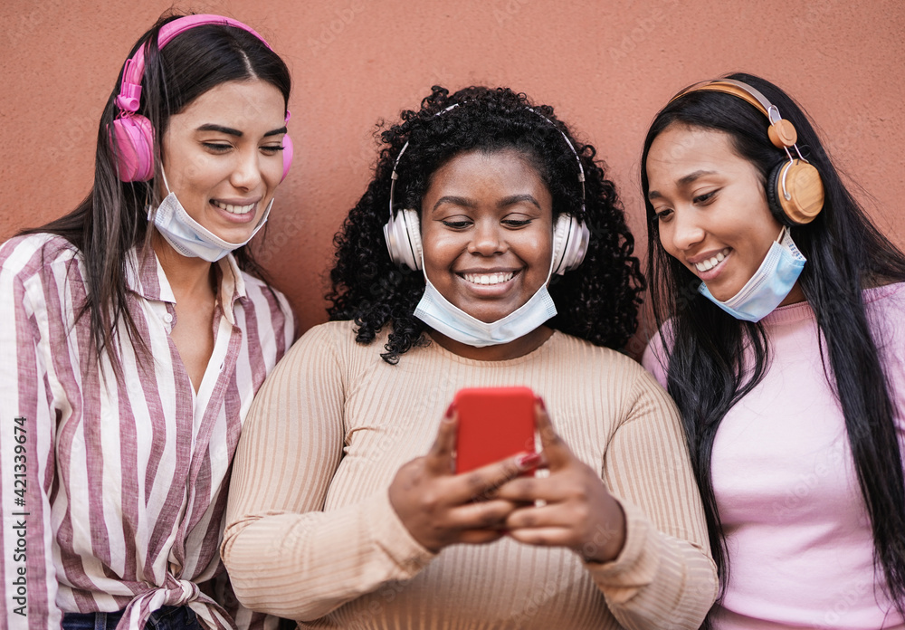 Young latin women with headphones wearing safety mask under chin for coronavirus while looking on smartphone - Millennial girls having social moment and enjoy technology outdoor Young latin women with headphones wearing safety mask under chin for coronavirus while looking on smartphone - Millennial girls having social moment and enjoy technology outdoor
