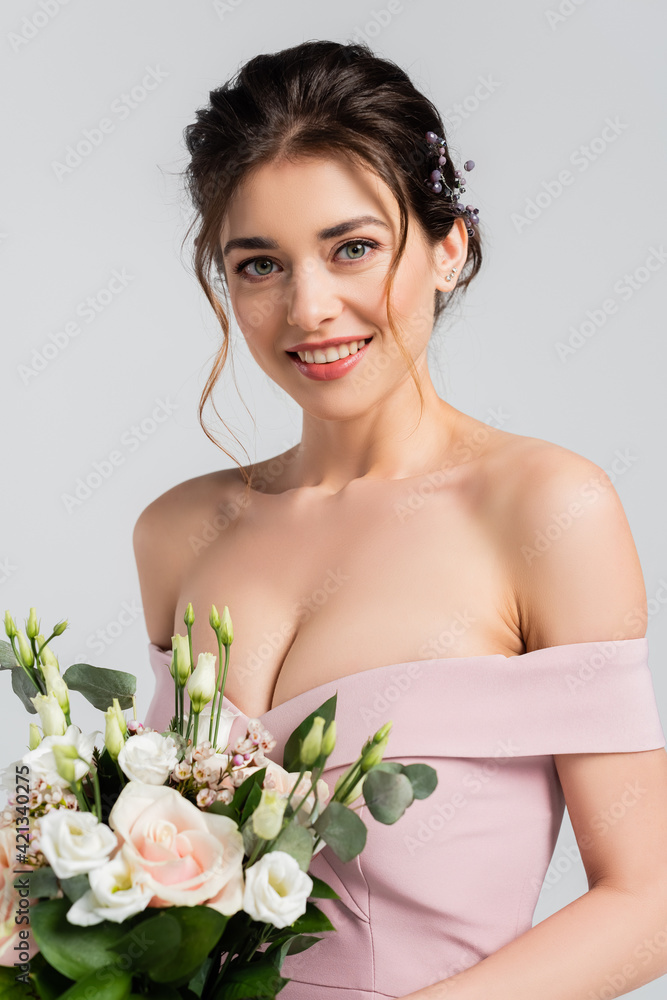 joyful bride smiling at camera while holding wedding bouquet isolated on grey joyful bride smiling at camera while holding wedding bouquet isolated on grey