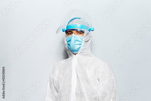 Portrait of a doctor wearing PPE suit against coronavirus and covid-19, on the background of white wall. Pandemic concept.