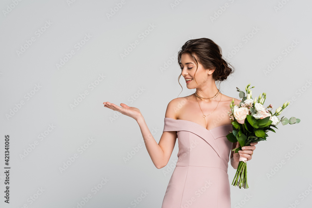 cheerful woman pointing with hand while standing with wedding bouquet isolated on grey cheerful woman pointing with hand while standing with wedding bouquet isolated on grey