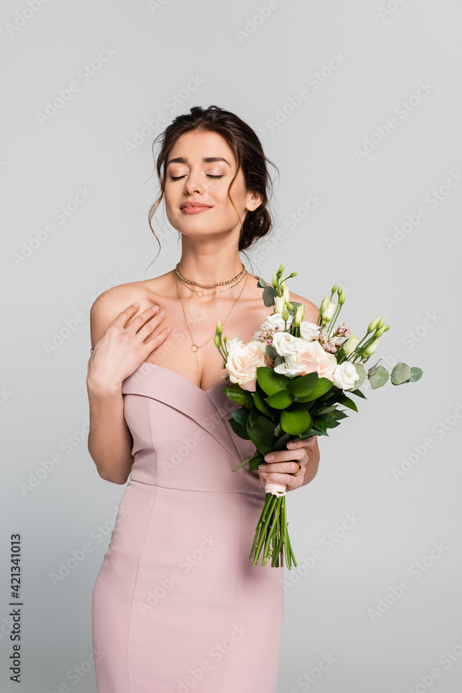 smiling woman holding wedding bouquet while standing with closed eyes isolated on grey smiling woman holding wedding bouquet while standing with closed eyes isolated on grey