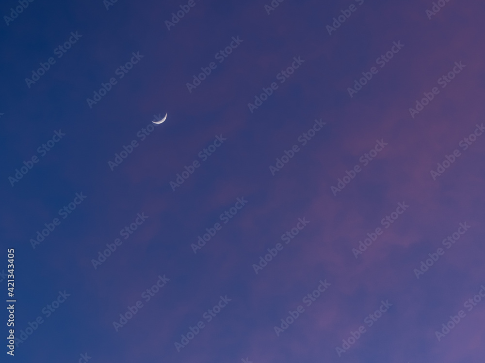 Fototapeta premium Luna pequeña fina y creciente en atardecer con nubes rosadas rojas