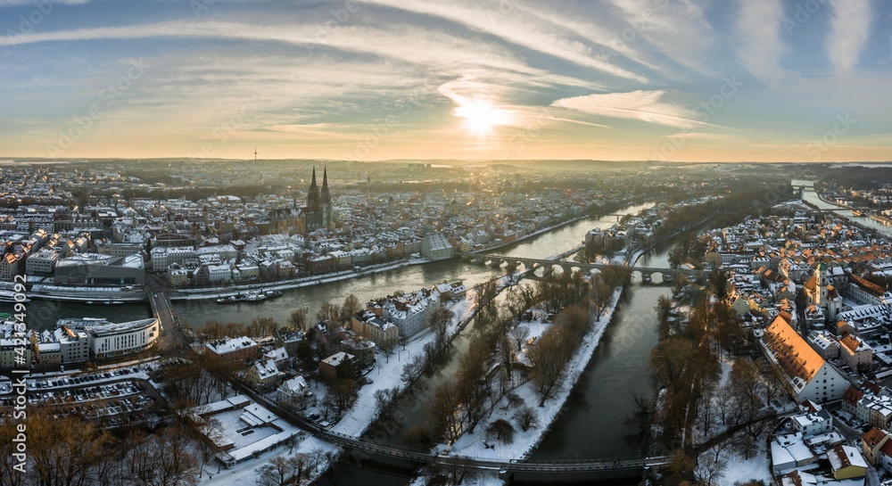 Panorama der Stadt Regensburg in Bayern mit dem Fluss Donau dem Dom und der steinernen Brücke im Winter mit Eis und Schnee bei Sonnenuntergang, Deutschland