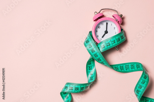 Pink alarm clock with teal measuring tape, top view. Healthy lifestyle, weight loss.